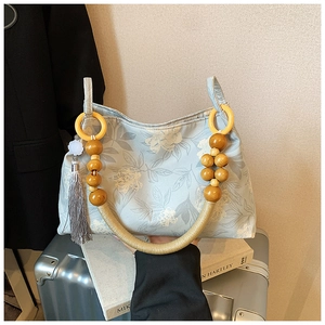 Detail of light blue floral canvas tote with beaded wooden handle and grey tassel decor