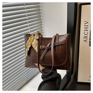 Detail of dark brown croc-embossed tote bag with decorative yellow patterned scarf