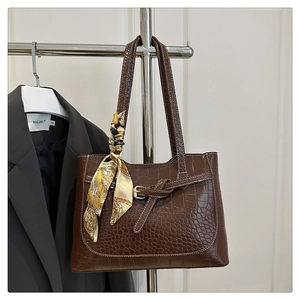 Macro detail of dark brown crocodile embossed tote bag with decorative silk scarf