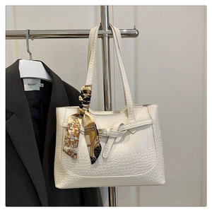 Detail of white crocodile pattern tote bag featuring a decorative silk scarf and strap