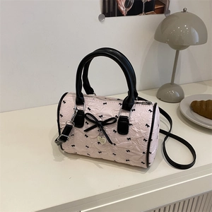 Pink seersucker Boston bag with black bow prints and a silver heart charm on a warm desk