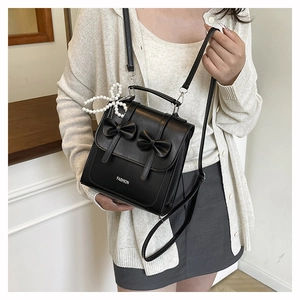 Detail of black crossbody bag with bow accents, pearl pendant and metal chain strap