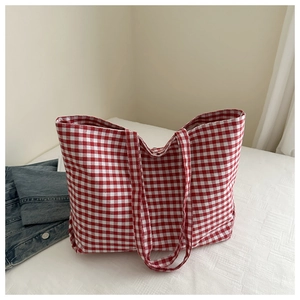 Top-down view of a red gingham canvas tote bag next to a blue denim jacket on white fabric