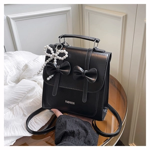 Detail of black faux leather bag featuring dual 3D bows, pearl pendant and metal logo