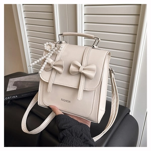 Close-up of cream fashion backpack with dual bows and elegant pearl charm detail
