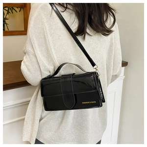 Detail of black patent leather crossbody bag with gold text and top handle on model