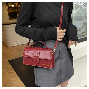 Detail of red patent leather crossbody bag with top handle and gold hardware detail