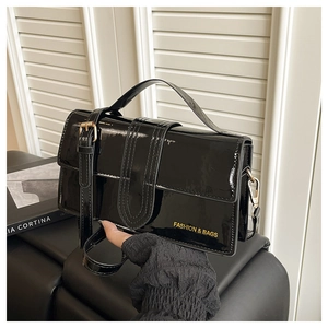 Detail of black patent leather handbag with gold metal buckles and fashion text logo
