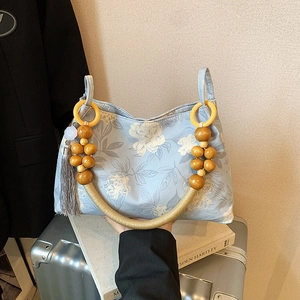 Light blue floral tote bag with wooden bead handle and tassel in a lifestyle setting