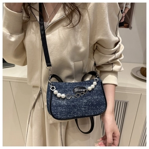 Detail of blue denim crossbody bag featuring pearl chain and metallic flower accents