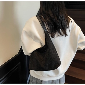 Close-up of black suede shoulder bag with rhinestone accents worn by model on stairs