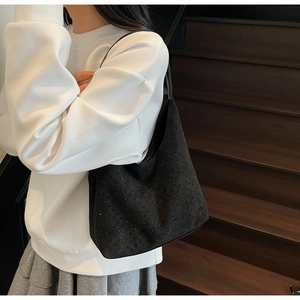 Détail du sac hobo noir orné de strass porté à l'épaule sur un sweat blanc