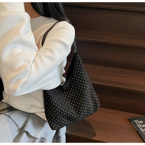 Détail du sac hobo noir à clous argentés porté avec un sweat blanc et jupe grise
