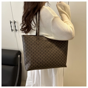 Detail of large brown tote bag with M-letter monogram and slim shoulder straps