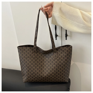 Close-up of the textured brown tote bag featuring a repeating 'M' monogram pattern
