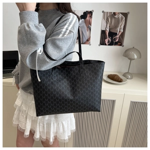 Macro detail of black tote bag with M-letter monogram pattern and white ribbon decor