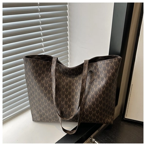 Macro detail of large brown tote bag with M-letter print and slim PU leather shoulder straps