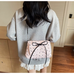 Quilted pink crossbody bag featuring black bow detail and metal chain strap for women