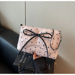 Detail einer hellrosa Faltenhandtasche mit schwarzen Schleifen und Metallkette