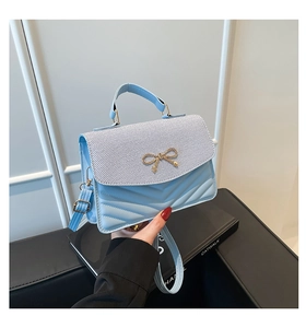 Détail d'un sac à main matelassé bleu clair avec un nœud doré et une poignée
