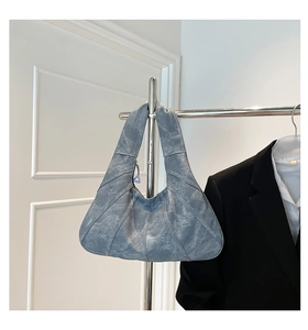 Detail view of denim blue shoulder bag with multi-stitch patchwork and crescent shape