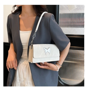 Close-up of a white shoulder bag with silver butterfly charm and chain strap details