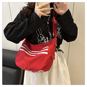 Détail du sac bandoulière en nylon rouge à rayures montrant sa grande capacité et matière