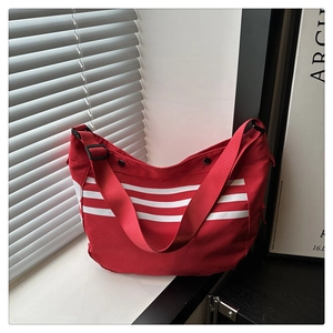 Détail du sac bandoulière en toile rouge avec trois bandes blanches et fermoirs aimantés