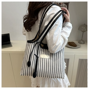 Detail of striped canvas tote bag showing black faux leather trim and drawstring detail
