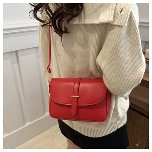 Detail of red matte leather crossbody bag featuring gold metal bar and adjustable strap