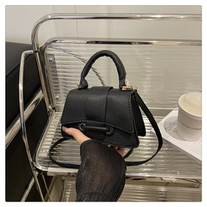 Close-up of black lychee grain mini handbag with unique crossbar buckle and handle