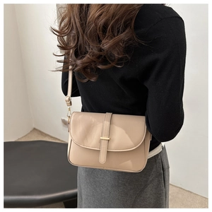Detail of beige faux leather crossbody bag featuring gold metal bar and flap closure