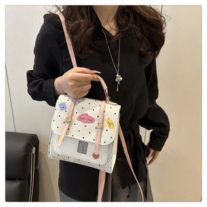 Detail of white polka dot handbag with cute cartoon patches and pink strap accents