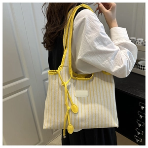 Detail of yellow and white striped canvas tote bag with thick shoulder straps and tassels