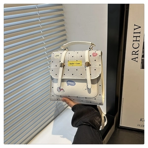 Detailed view of a white polka dot backpack with colorful stickers and metal buckle