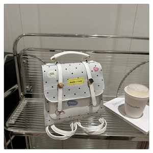 Close-up of small white polka dot backpack with decorative patches on a stylish display