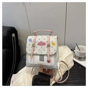 Close-up of a white polka dot mini backpack featuring pink leather flaps and decorative patches