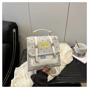 Detail view of a white polka dot handbag with creative patches and flap closure on a table