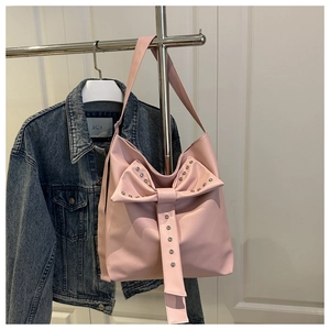 Detailed view of pink bow decoration and metal rivets on the glossy leather shoulder bag