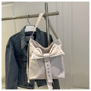 Close-up of ivory shoulder bag featuring oversized bow detail and silver stud accents