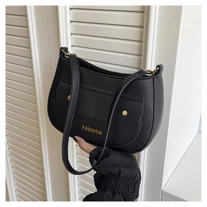 Detail of black litchi grain leather shoulder bag with golden FASHION buckle and studs