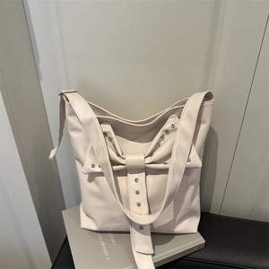 Sac fourre-tout beige chic avec grand nœud et clous argentés sur fond de livre moderne