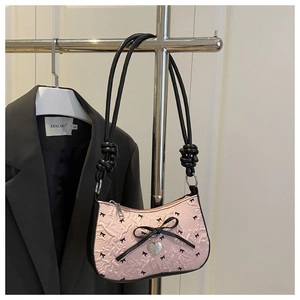 Close-up of pink crescent underarm bag featuring ribbon bows and silver heart charm