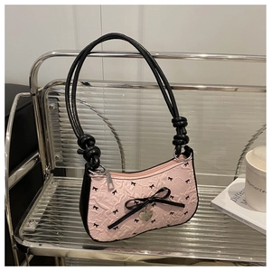 Detailed close-up of pink quilted baguette bag featuring black bows and a silver heart charm