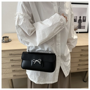 Vue détaillée du sac bandoulière noir avec nœud argenté sur une blouse blanche