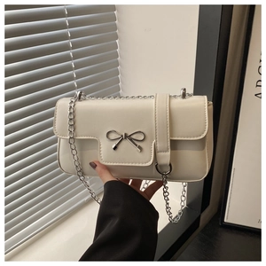 Détail d'un sac bandoulière en similicuir crème avec nœud argenté et chaîne élégante