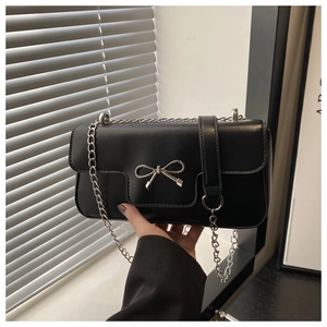 Détail du sac noir minimaliste à chaîne avec un nœud en métal argenté et un rabat chic