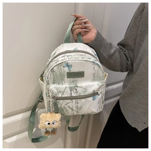 Detail eines Mini-Rucksacks mit Schmetterlingsmuster und Plüschmonster-Anhänger