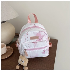 Detailansicht weißer Mini-Rucksack mit Schmetterlingsdruck und Plüschanhänger auf Holztisch