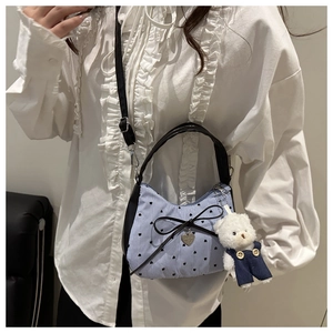 Detail of blue striped tote bag featuring heart patterns, a black bow, and a plush bear charm